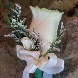 White rose boutonniere with small filler flowers and a satin ribbon bow