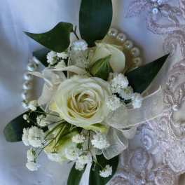 White rose corsage with baby's breath and dark green leaves