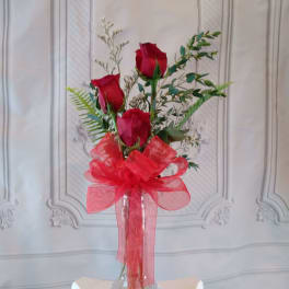 Three red roses in a clear glass vase with a large red bow