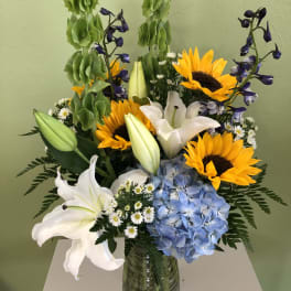 Bouquet of sunflowers, white lilies, blue hydrangea, and purple flowers in a glass vase