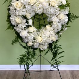 Heart-shaped white floral wreath on a stand with trailing greenery