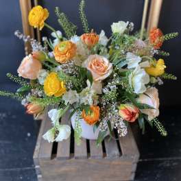Mixed bouquet of peach, yellow, and white flowers in a white vase
