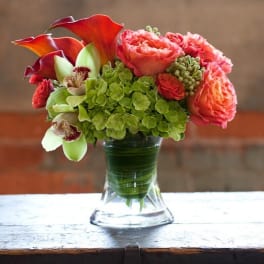 Bouquet of coral roses, green hydrangea, and calla lilies in a glass vase