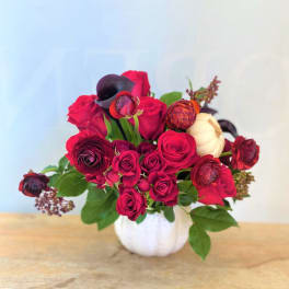 Red roses and dark ranunculus in a white pumpkin vase