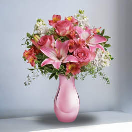 Pink roses and lilies arranged in a pink glass vase