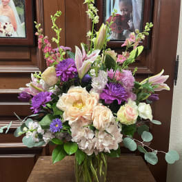 Mixed bouquet of pink, purple, and cream flowers in a glass vase