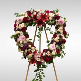 Heart-shaped floral wreath on a wooden stand with red, pink, and white flowers