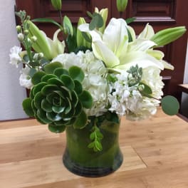 White lilies and hydrangeas in a green glass vase with succulents.