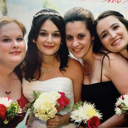 Four women in formal dresses holding small bouquets of white and red flowers