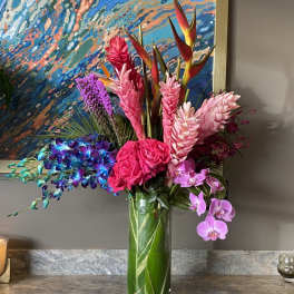 Tropical bouquet in a tall glass vase with pink orchids and bright mixed blooms