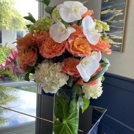 Orange roses and white orchids arranged in a tall glass vase