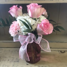 Pink roses and white hydrangeas in a purple glass vase with a pink ribbon