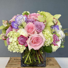 Mixed bouquet of pink and lavender roses with pale green hydrangeas in a glass vase