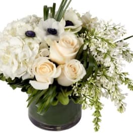 White floral arrangement in a dark glass vase with roses and anemones
