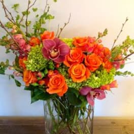 Orange roses and purple orchids in a clear glass vase
