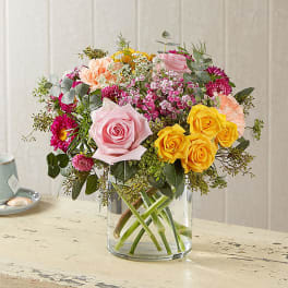 Mixed bouquet of pink, yellow, and peach flowers in a clear glass vase