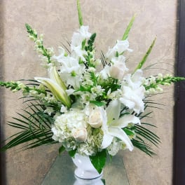 White floral arrangement in a white vase with lilies and roses