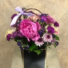 Pink and purple flower basket with a ribbon on a black box