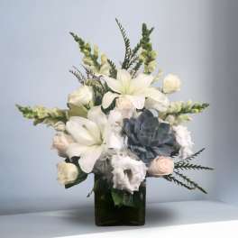 White lilies and roses arranged in a dark glass vase with a blue succulent