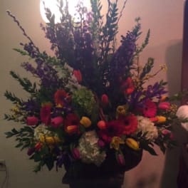 Tall mixed flower arrangement with bright tulips and gerbera daisies in a dark vase