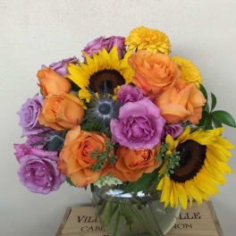 Bouquet of orange and purple roses with sunflowers in a glass vase