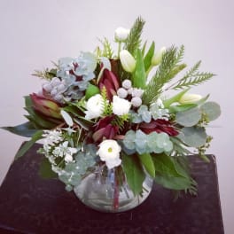 Mixed floral arrangement in a round glass vase with white blooms and burgundy accents