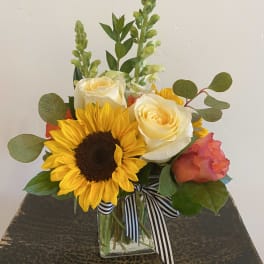 Sunflower and rose bouquet in a clear glass vase with striped ribbon