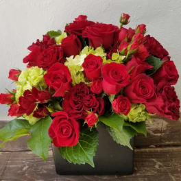 Red roses and lime-green flowers arranged in a black square vase