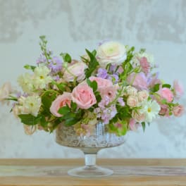 Pink and white floral arrangement in a glass compote vase
