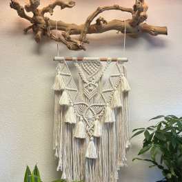 Macrame wall hanging suspended from a driftwood branch with potted plants below