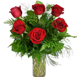 Red roses arranged in a clear glass vase with green foliage