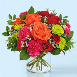 Mixed bouquet of orange, red, and pink flowers in a clear glass vase