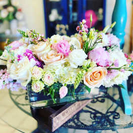 Pastel bouquet of roses, ranunculus, and small pink blooms in a low container