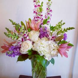 Tall bouquet of pink lilies, white roses, and purple flowers in a glass vase