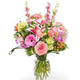 Mixed pink and peach flowers arranged in a clear glass vase