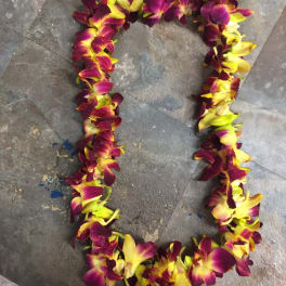 A purple and yellow orchid lei laid in a loop on a stone floor.