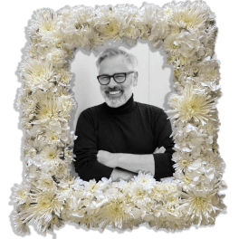 White floral frame surrounding a portrait of a smiling man