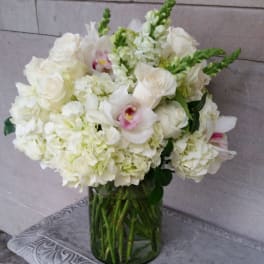 White floral arrangement in a glass vase with pink orchid accents