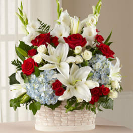 Basket arrangement of red roses, white lilies, and blue hydrangeas