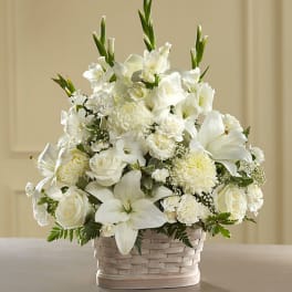 White floral arrangement in a woven basket with lilies and roses