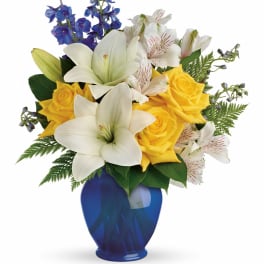 Bouquet of white lilies, yellow roses, and blue flowers in a blue vase