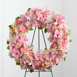 Pink floral wreath with lilies, roses, and carnations on a black stand