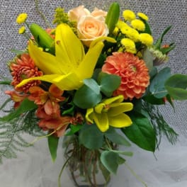 Mixed bouquet with yellow lilies, peach roses, and orange blooms in a glass vase