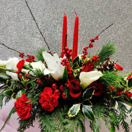 Holiday arrangement with red and white flowers, candles, and pinecones