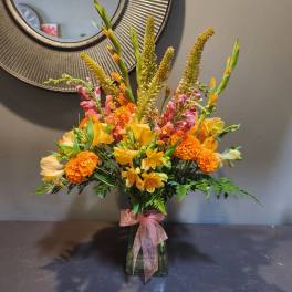 Orange and yellow mixed bouquet in a glass vase with a pink ribbon