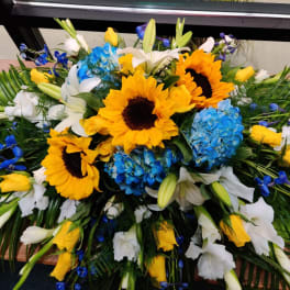 Large floral spray with sunflowers, blue hydrangeas, white lilies, and yellow roses