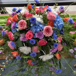 Colorful floral casket spray with roses, hydrangeas, and daisies