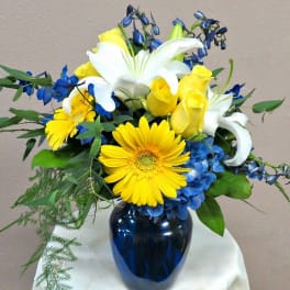 Bouquet of yellow roses, white lilies, and blue flowers in a dark vase