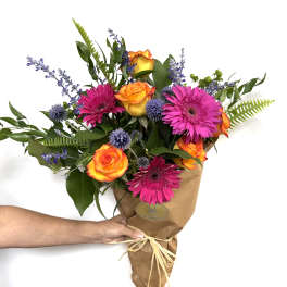 Bouquet of orange roses, pink gerberas, and purple accents in brown paper