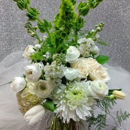 Tall white and green flower arrangement with roses, ranunculus, tulips, and Bells of Ireland in a clear glass vase